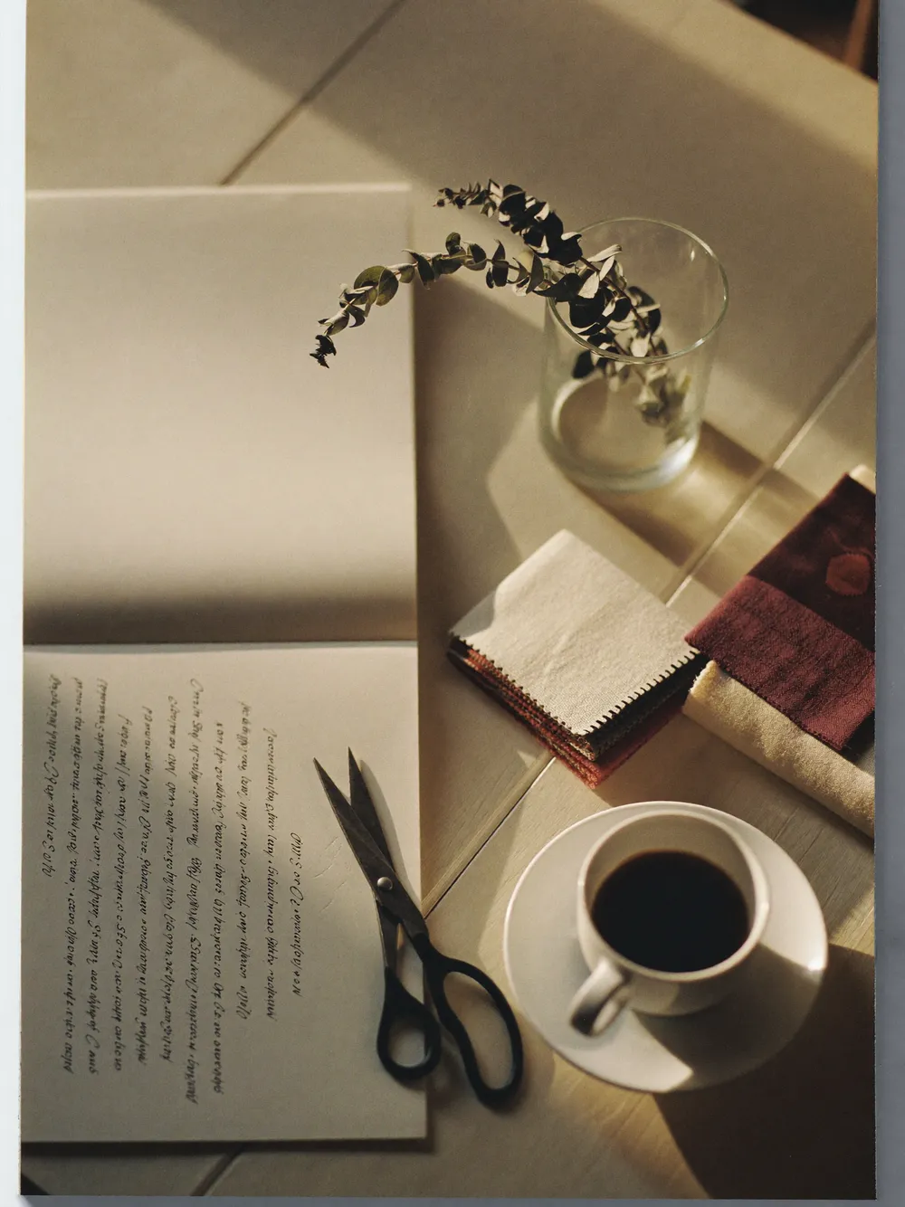 Schreibtisch mit aufgeschlagenem Notizbuch, Kaffeetasse und Stoffmustern im Morgenlicht.